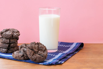 Glass of fresh milk with a pile of crunchy baked chocolate sugar cookies on wooden table with dark blue dinner napkin on pink background. Ideas of school breakfast or fast snack for students.