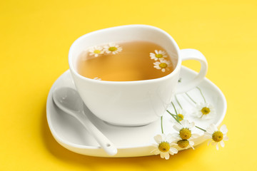Delicious chamomile tea in cup on yellow background