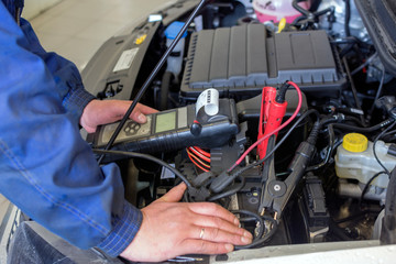 A professional car mechanic works in a car service. Mechanic service using Multimeter to check the voltage level in a car battery Car diagnostics. © Дмитрий Ульяненко