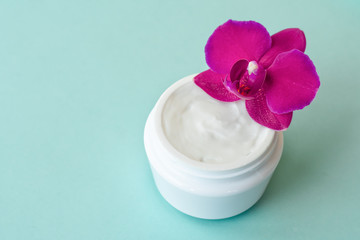 Cream in white jar on mint background with beautiful bright magenta orchid flowers. Rejuvenating cream with orchid extract for moisturizing skin. Eco cosmetic product