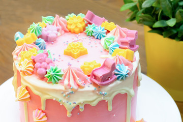 Party cake covered by pink and white cream with colorful meringue, chocolate bears, flowers and...