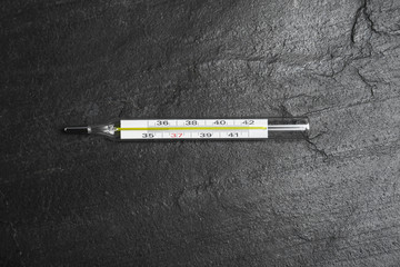Mercury thermometer on black slate background, top view