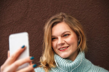 young woman in a blue sweater uses a mobile phone on a dark background close up