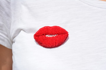 Brooch from beads in the form of red lips dressed on a white female T-shirt