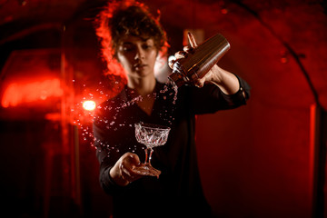 young handsome woman pouring drink from metal shaker into glass.