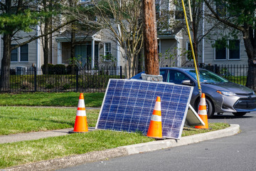 Cracked solar panel on the ground near a utility pole that they fell from with orange warning cones nearby