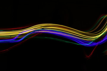 Long exposure photograph of neon multi colour in an abstract swirl, parallel lines pattern against a black background. Light painting photography.