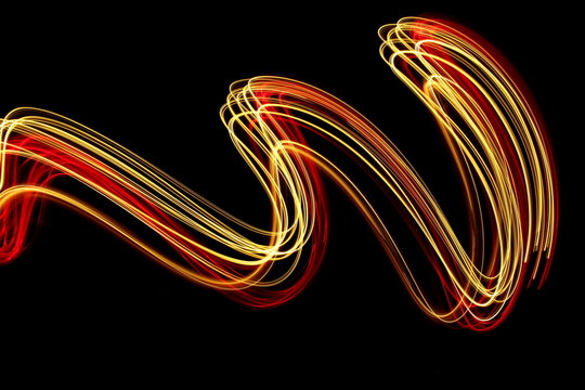Long exposure photograph of neon red and gold colour in an abstract swirl, parallel lines pattern against a black background. Light painting photography.