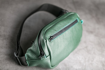 Belt bag made of dark green textured leather, banana on a gray background.