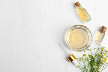 Flat lay composition with chamomile essential oil on white wooden background. Space for text