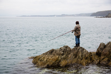 Fototapeta na wymiar Fisherman catches fish on the rocks