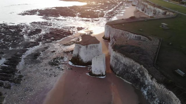 Aerial of White cliffs on beach with white sand and pink sky at sunrise in England 4k cinamatic person walking on beach on goldan sand