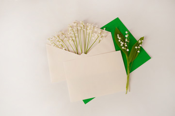 Flower arrangement. An envelope, a blank sheet of paper and spring lilies of the valley (Convallaria majalis) on a pastel beige background. Free space for your text.