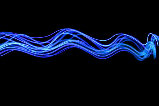 Long exposure photograph of neon blue colour in an abstract swirl, parallel lines pattern against a black background. Light painting photography.