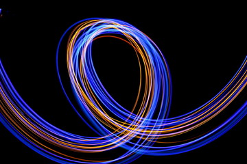 Long exposure photograph of neon blue and gold colour in an abstract swirl, parallel lines pattern against a black background. Light painting photography.