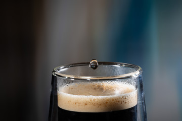 Coffee splash. Reaction of a falling drop on the hot, steaming and frothy coffee surface in a modern glass transparent cup. Studio photo with matching colored background