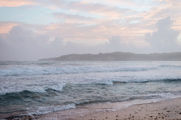 Fototapeta na wymiar Pink-blue sky. Low clouds and fog over the ocean. Foaming waves roll ashore