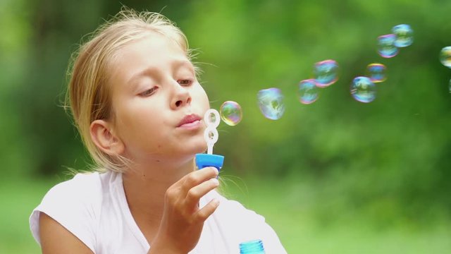 Girl playing with soap bubbles outdoor. Nine-year-old girl plays with soap bubbles in the summer garden. Slow motion.