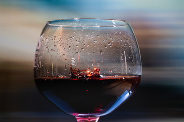 Red wine splash. Reaction of a falling drop on a red wine  surface in a big half filled modern glass transparent pint. Studio photo with matching   colored background. Beautiful drop splash
