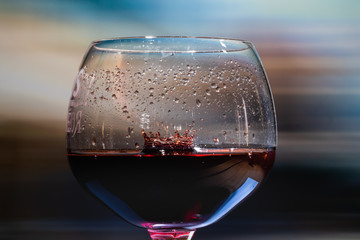 Red wine splash. Reaction of a falling drop on a red wine  surface in a big half filled modern glass transparent pint. Studio photo with matching   colored background. Beautiful drop splash