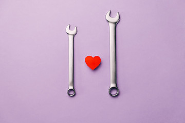 Creative flat lay composition with little red heart, two combination wrenches on violet background...
