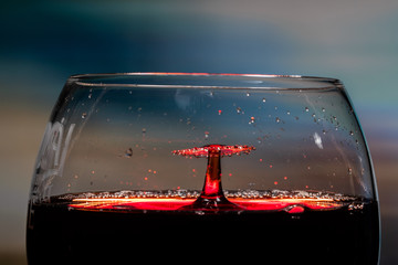 Red wine splash. Reaction of a falling drop on a red wine  surface in a big half filled modern...