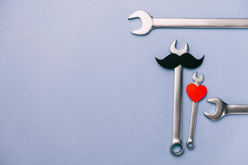 Fathers day masculinity concept blog. Flat lay composition with red heart, retro stylish black funny paper moustache, combination wrenches on blue background with copy space. Minimal style