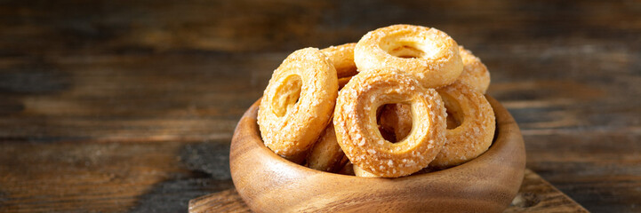 Puff pastry sprinkle with sugar in a wooden bowl on a brown wooden background. Cookies sprinkle with sugar close-up. Sweet pastries. Banner