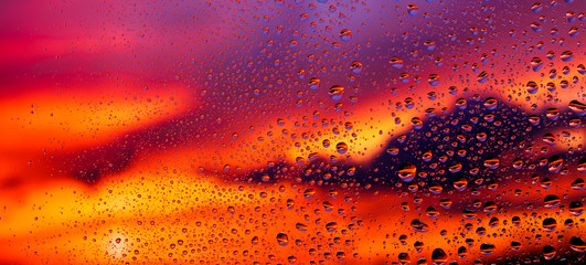 Raindrops on the glass against the background of a bright summer sunset 