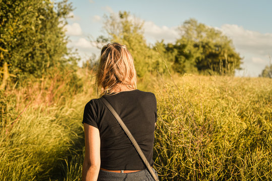 Young beautiful woman walking in field at sunset from behind.