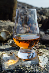 Tasting glass of Scotch whisky and sea shore during low tide, smoky whisky pairing with oysters