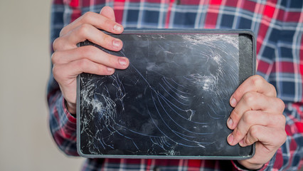 A man holds a tablet with a broken screen