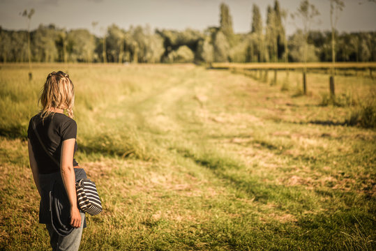 Young beautiful woman standing in field in summer from behind.