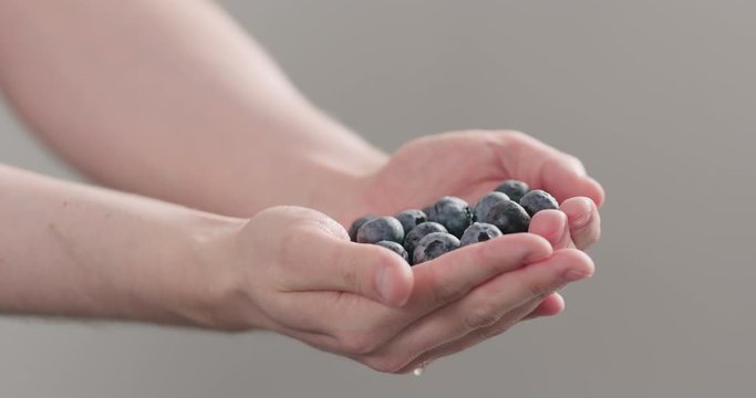 Slow motion man hands show wet washed ripe blueberries on neutral background
