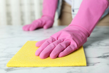 Woman in gloves wiping white marble table with rag indoors, closeup