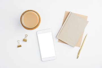 Flat lay home office desk with paper notebook, smartphone with blank screen mockup, cup of coffee and office supplies on white background. Top view modern feminine workspace, minimalist style.