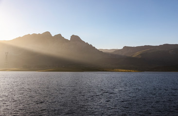 Landscape of sun rays trespassing the mountains and going towards the water of the lake in the countryside of the north of Spain.