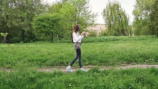 woman in sneakers walks on a dirt road. Girl dressed in jeans and sneakers is walking through the park.