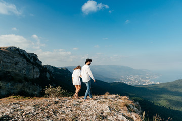 Obraz premium Attractive young loving couple of man in white shirt and blue jeans with girl in dress on sunny outdoor background in the green mountain landscape