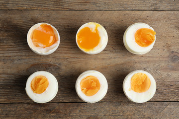Different readiness stages of boiled chicken eggs on wooden table, flat lay