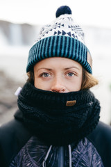 Portrait of young woman in a warm clothes. She wears white hat with ornament and warm cozy scarf.