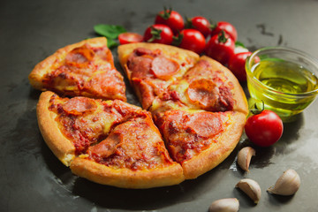 Top view of hot pepperoni pizza,Tasty pepperoni pizza and cooking ingredients tomatoes basil on black background.