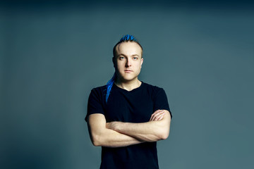 Portrait of a young man with an unusual hairstyle of mohawk from blue braids in sportswear posing full face on a gray