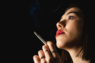 Obraz premium Low key close-up young woman smoking cigarette on black background. 