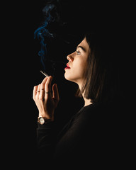 Obraz premium Low key close-up young woman smoking cigarette on black background. 