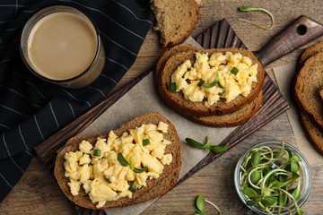 Tasty scrambled egg sandwiches served on wooden table, flat lay