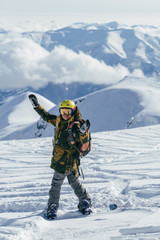 Gudauri ski resort in Georgia. Girl wih bright helment and colorful backpack on a snowboard admires snow-capped mountain peaks and clouds which hanging low overhead.  She is going to freeride.