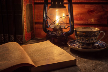Reading a book in the light of an old hand-held kerosene lamp glows softly in a dark room on the table. Vintage style. The light in the darkness. Atmospheric photo in the loft style.