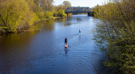 Two men are swimming on a paddleboard on the spring river.I can't see his face.