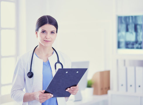 Young smiling female doctor with stethoscope holding a folder at doctor's office